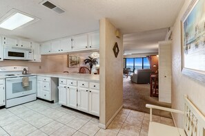 A kitchen with white cabinets, a microwave, and a stove. There is a dining area with a chair and a table. - Ocean view from the master bedroom and living room with a spacious balcony (Fernandina Beach)