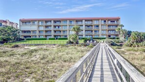 A multi-story hotel with a red-tiled roof, balconies, and a wooden boardwalk leading to the entrance. - Ocean view from the master bedroom and living room with a spacious balcony (Fernandina Beach)