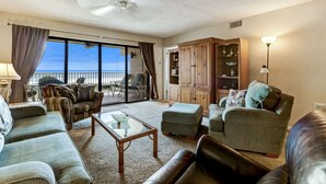 A spacious living room with a large sliding glass door leading to a balcony, furnished with a sofa, armchairs, a coffee table, and a cabinet. - Ocean view from the master bedroom and living room with a spacious balcony (Fernandina Beach)
