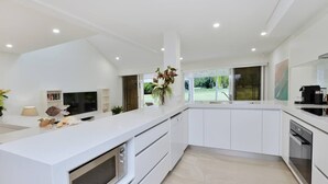 Een moderne keuken met witte kastjes, een inbouwoven en een groot raam met uitzicht op de omgeving.