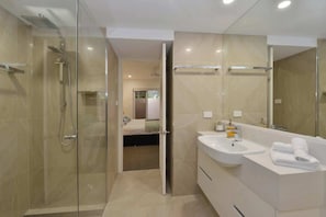 Un bagno moderno con doccia vetro, uno specchio grande e un mobile lavabo bianco con lavandino e asciugamano.