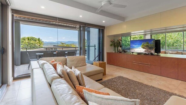 A modern living room with a sofa, television, and a view of the outdoors. - Villa On The Hill —Spacious Tropical Panorama (Port Douglas)