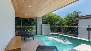 A modern outdoor pool area with a waterfall feature, a lounge chair, and a table. - Villa On The Hill —Spacious Tropical Panorama (Port Douglas)