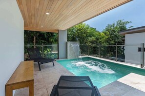 A modern outdoor pool area with a waterfall feature, a lounge chair, and a table.
