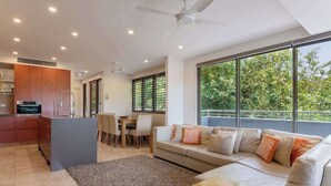 A modern living space with a kitchen, dining area, and a large window with a view of greenery. - Villa On The Hill —Spacious Tropical Panorama (Port Douglas)