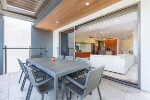 An outdoor dining area with a table and chairs, a wooden ceiling, and a view into the house.