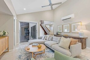 Un salon moderne avec un canapé, une table basse, un ventilateur de plafond et un escalier menant à un autre niveau.