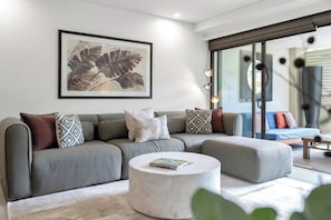 A modern living room with a grey sectional sofa, a round coffee table, and a framed botanical print on the wall. - Poolside at Temple Resort: A Lush Tropical Escape (Port Douglas)