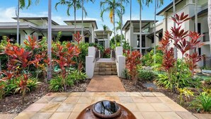 Un moderno resort con un sendero central que conduce a una escalera, rodeado de plantas tropicales y palmeras.