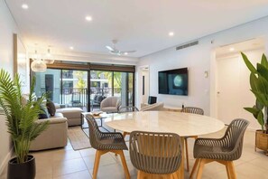 Una sala de estar moderna con una mesa de comedor redonda, asientos cómodos, un televisor de pantalla plana y ventanas grandes.
