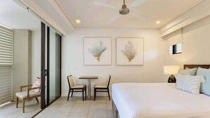 A hotel room with a bed, two chairs, a small table, a ceiling fan, and two wall-mounted artworks. - Sunny Swim-out Serenity with Direct Beach Access (Port Douglas)