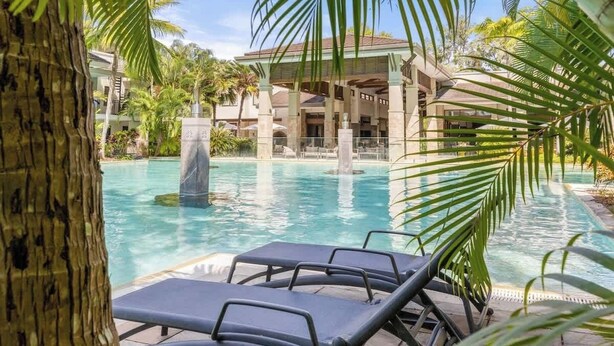 A pool area with lounge chairs, palm trees, and a building with a tiled roof. - Sunny Swim-out Serenity with Direct Beach Access (Port Douglas)