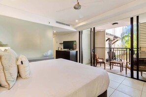 A bedroom with a bed, a TV, a desk, and a balcony with chairs. - Sunny Swim-out Serenity with Direct Beach Access (Port Douglas)