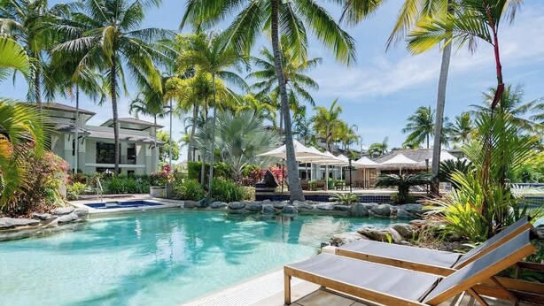 Un espace piscine avec des chaises longues, des palmiers et une maison en arrière-plan.
