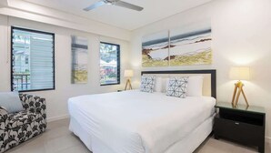 Une chambre à coucher avec un grand lit, un ventilateur de plafond, un canapé et des œuvres d’art accrochées aux murs.