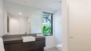 Un baño moderno con un tocador oscuro, un espejo grande y una ventana con persianas.