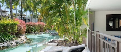 A pool area with lounge chairs, palm trees, and a small waterfall.