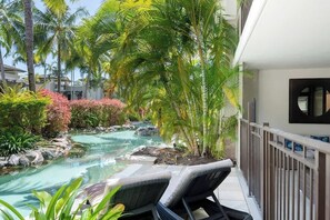 A pool area with lounge chairs, palm trees, and a small waterfall.