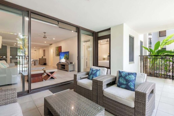 A modern living room with a glass door leading to a balcony, a sofa set, and a television.