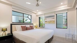 Un dormitorio moderno con una cama grande, mesitas de noche, ventilador de techo y una ventana con persianas.