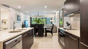 A modern kitchen with a central island, built-in appliances, and a dining area with a view. - The Plunge Pool Residence—Private Resort Living (Port Douglas)