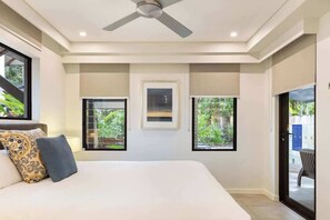 A bedroom with a bed, ceiling fan, large windows, and a view of greenery outside.