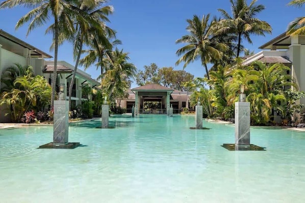 A resort pool with palm trees, a covered area, and a building in the background.