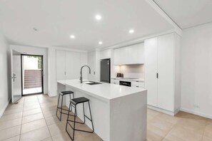 Una cucina moderna con mobili bianchi, un'isola centrale con sgabelli da bar e illuminazione a incasso.