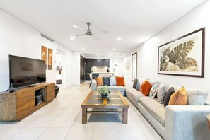 A modern living room with a flat-screen TV, a wooden coffee table, a sofa with cushions, and a ceiling fan.