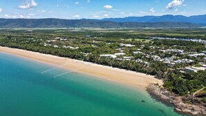 An aerial view of a coastal area with a beach, a golf course, and a residential area with houses.
