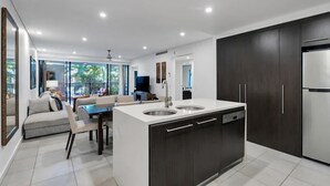 A modern kitchen with dark cabinetry, a central island with a sink, and a dining area with a sofa and table.