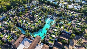 Eine Vogelperspektive auf ein Resort mit mehreren bungalowsähnlichen Unterkünften, einem zentralen Swimmingpool und umgebender Bepflanzung.