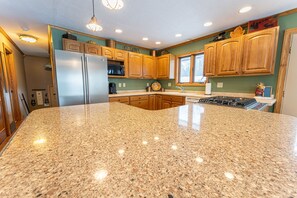 A kitchen with granite countertops, wooden cabinets, a stainless steel refrigerator, and a gas stove. - Farmer Lake Lodge:  Fall Colors & Lake Views | Lakefront Lodge | Sleeps 12 (Little Lake)