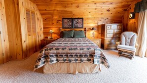 Ein Schlafzimmer einer Holzhütte mit einem Bett, einer Kommode, einem Stuhl und zwei Wandleuchten.