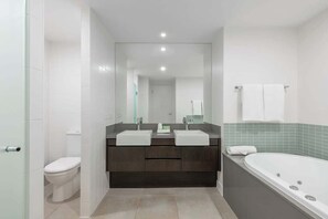 A modern bathroom with a dual sink vanity, a toilet, and a bathtub.