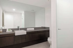 A modern bathroom with a large mirror, dark wood vanity, white sink, and a toilet. - Swim-out Tropical Getaway by Four Mile Beach (Port Douglas)