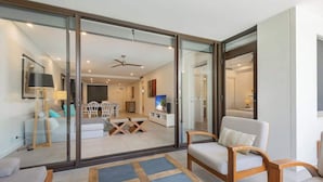 A modern living room with a glass sliding door leading to a dining area, a ceiling fan, and a flat-screen TV. - Swim-out Tropical Getaway by Four Mile Beach (Port Douglas)
