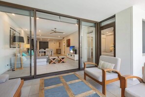 A modern living room with a glass sliding door leading to a dining area, a ceiling fan, and a flat-screen TV. - Swim-out Tropical Getaway by Four Mile Beach (Port Douglas)
