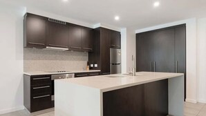 A modern kitchen with dark cabinetry, a central island, and a tiled backsplash. - Swim-out Tropical Getaway by Four Mile Beach (Port Douglas)