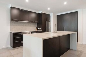 A modern kitchen with dark cabinetry, a central island, and a tiled backsplash. - Swim-out Tropical Getaway by Four Mile Beach (Port Douglas)
