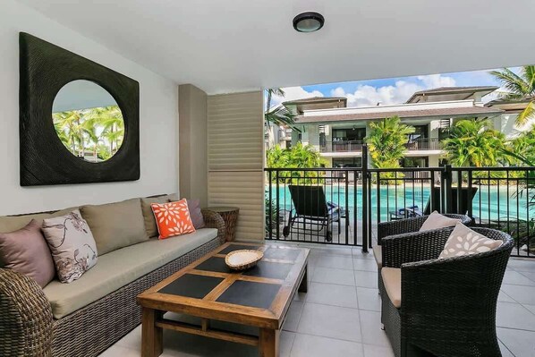 Ein Balkon mit Blick auf einen Pool, eine Couch, ein Couchtisch und Korbmöbel.