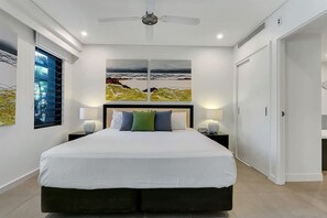 Ein modernes Schlafzimmer mit einem großen Bett, zwei Nachttischen, einem Deckenventilator und Kunstwerken an der Wand.