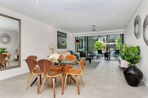 A modern dining area with a glass table and wooden chairs, a large mirror, and a view into the living room. - Aqua Oasis: Swim-out Resort Sanctuary (Port Douglas)