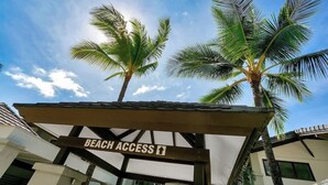 A beach access sign, palm trees, and a building with a modern architectural style.