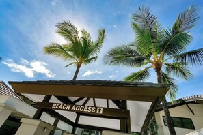 Segnale di accesso alla spiaggia, palme e un edificio in stile architettonico moderno.