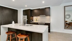 A modern kitchen with dark cabinetry, a white countertop, and two wooden stools.