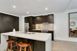 A modern kitchen with dark cabinetry, a white countertop, and two wooden stools. - Aqua Oasis: Swim-out Resort Sanctuary (Port Douglas)