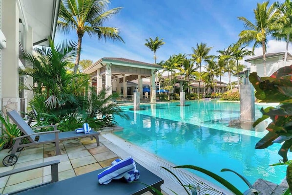 A pool area with lounge chairs, palm trees, and a covered seating area.