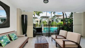 A room with a sofa, a coffee table, and a view of a pool and buildings. - Poolside Bliss: A Modern Resort Sanctuary (Port Douglas)