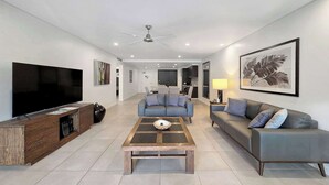 A modern living room with a flat-screen TV, a wooden coffee table, a blue sofa, a grey sofa, a ceiling fan, and a framed plant. - Poolside Bliss: A Modern Resort Sanctuary (Port Douglas)